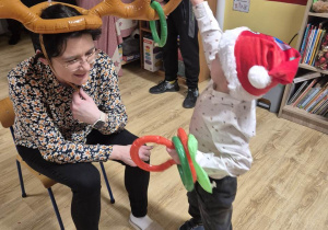 Chłopiec próbuje założyć koło na dmuchane rogi Mikołaja, które ma na głowie mama.