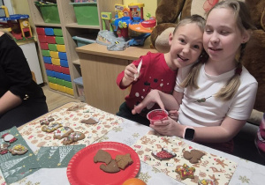 Brat z siostrą siedzą przy stole i ozdabiają pierniczki.