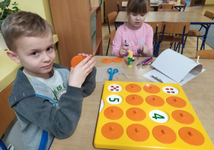 chłopiec gra w grę matematyczną, obok siedzi dziewczynka i maluje