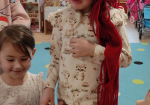 dziewczynka stoi przy stoliku z owocami, ma zasłonięte oczy, obok inne dzieci