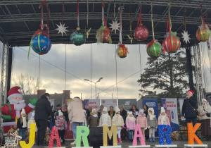 dzieci stoją na scenie , występuja podczas Jarmarku bożonarodzeniowego