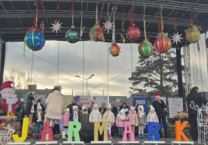 dzieci stoją na scenie , występuja podczas Jarmarku bożonarodzeniowego