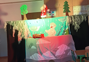 dzieci siedzą na dywanie oglądają przedstawienie, przed mini scenografia