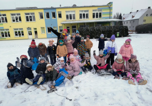 grupa dzieci i nauczycielka pozujądo wspólnego zdjęcia w ogrodzie , za nimi budynek przedszkola