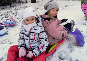 dwie dziewczynki siedzą na jednych sankach