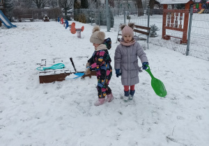 dwie dziewczynki w ogrodzie przedszkolnym, w rękach mająjabłuszka do zjazdów na śniegu