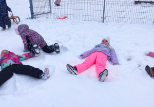 grupa dzieci w przedszkolnym ogrodzie , bawią się na śniegu, robią "aniołki"