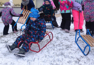 dzieci na górce w przedszkolnym ogrodzie , jedne biegają, inne zjeżdzająna sankach