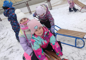 dzieci w przedszkolnym ogrodzie , bawią się na śniegu, na pierwszym planie dziewczynkia na sankach