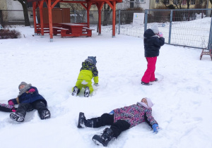 grupa dzieci w przedszkolnym ogrodzie , bawią się na śniegu, robią "aniołki"