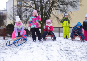 dzieci na górce w przedszkolnym ogrodzie , jedne stoją, inne zjeżdzająna sankach