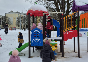 grupa dzieci w przedszkolnym ogrodzie , bawią się na śniegu i urżądzeniach placu zabaw