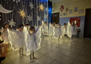 dziewczynki w strojach aniołków wykonują taniec na występie, mająna sobie świecące pelerynki