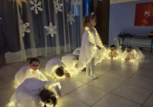 dziewczynki w strojach aniołków wykonują taniec na występie, mająna sobie świecące pelerynki