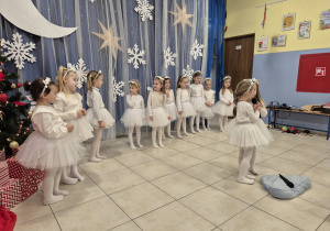 dwie dziewczynki w białych strojach mówią wiersz do mikrofonu, w tle inne dziewczynki