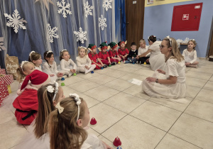 dzieci przebrane za aniołki i elfy siedzą na podłodze, grająna dzwonkach, obok nauczycielki