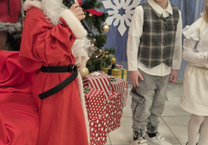 dziecko przebrane za św. Mikołaja mówi wiersz do mikrofonu w tle inne dzieci