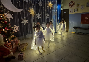 dziewczynki w strojach aniołków wykonują taniec na występie, mająna sobie świecące pelerynki