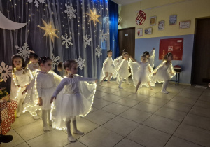 dziewczynki w strojach aniołków wykonują taniec na występie, mają na sobie świecące pelerynki