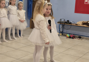 dwie dziewczynki w białych strojach mówią wiersz do mikrofonu