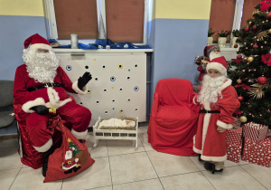 dziecko przebrane za św. Mikołaja stoi obok dorosłego przebranego za św. Mikołaja, w tle choinka