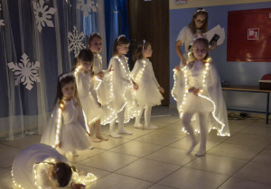 dziewczynki w strojach aniołków wykonują taniec na występie, mają na sobie świecące pelerynki