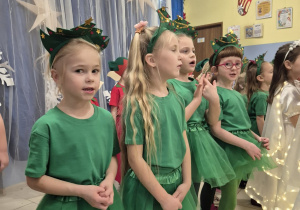 grupa dzieci przebranych za choineczki podczas występu światecznego, w tle zimowa dekoracja