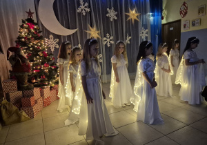 grupa dziewczynek ubranych na biało, mają świecące narzutki, tańczą na występie
