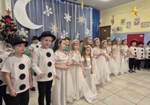 grupa dzieci przebranych za bałwanki i anioły podczas występu światecznego, w tle zimowa dekoracja