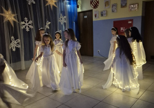 grupa dziewczynek ubranych na biało, mają świecące narzutki, tańczą na występie