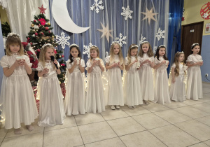 grupa dziewczynek przebranych za aniołki, w rękach mają kubeczki ze "sniegiem", występują przed rodzicami