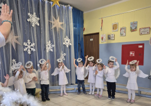 grupa dzieci , niektóre przebrane za aniołki, pozostałe elegancko ubrane prezentuje rodzicom świąteczne przedstawienie