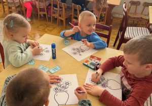 grupa dzieci przy stoliku w bibliotece koloruje obrazki z kwiatami