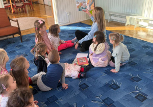 dzieci siedzą na dywanie słuchają opowiadań czytanych przez bibliotekarkę