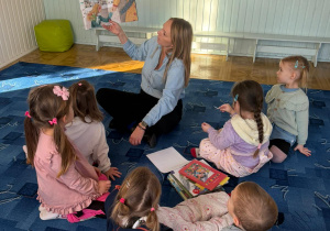 dzieci siedzą na dywanie słuchają opowiadań czytanych przez bibliotekarkę