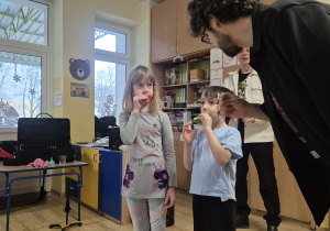 dwoje dzieci próbuje grać na piszczałkach, obok muzyk