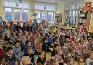 przedszkolaki zgromadzone w sali, siedzą na podłodze oglądają występ muzyczny