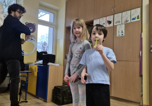 dwoje dzieci próbuje grać na piszczałkach, obok muzyk