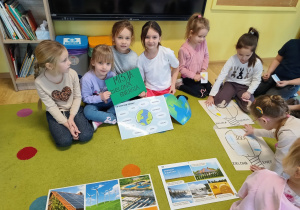 grupa dzieci siedzi na dywanie przed nimi plansze edukacyjne i wykonane przez nie zadania projektowe