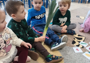 grupa dzieci siedzi na dywanie , jeden z chłopców trzyma w rękach pora