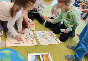 grupa dzieci siedzi na dywanie przed nimi plansze edukacyjne i wykonane przez nie zadania projektowe