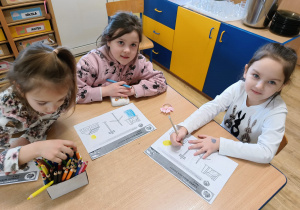 grupa dzieci przy stoliku wykomuje karty pracy