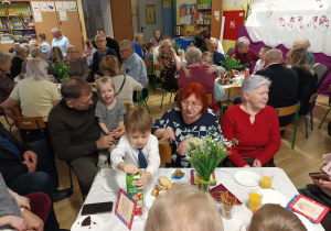 Po części artystycznej, dziadowie z wnuczętami siedzą przy stolikach podczas słodkiego poczęstunku. Celebrują wspólny czas i pozują do zdjęć.
