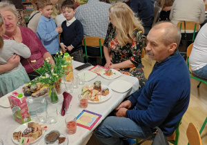 Po części artystycznej, dziadowie z wnuczętami siedzą przy stolikach podczas słodkiego poczęstunku. Celebrują wspólny czas i pozują do zdjęć.