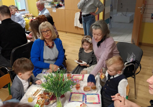 Po części artystycznej, dziadowie z wnuczętami siedzą przy stolikach podczas słodkiego poczęstunku. Celebrują wspólny czas i pozują do zdjęć.