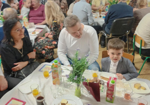 Po części artystycznej, dziadowie z wnuczętami siedzą przy stolikach podczas słodkiego poczęstunku. Celebrują wspólny czas i pozują do zdjęć.