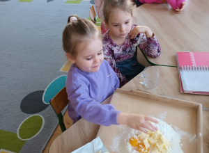 Dzieci siedzą przy stoliczku i przygotowują ciasto na ciasteczka.