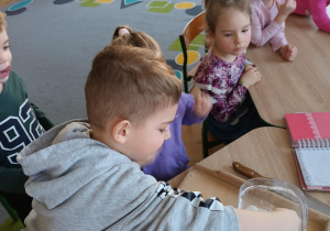 Dzieci siedzą przy stoliku i przygotowują ciasto na ciasteczka.