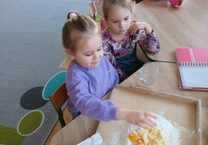 Dzieci siedzą przy stoliku i przygotowują ciasto na ciasteczka.