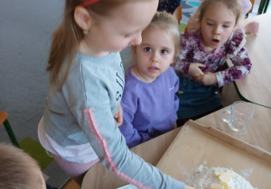 Dzieci siedzą przy stoliku i przygotowują ciasto na ciasteczka.